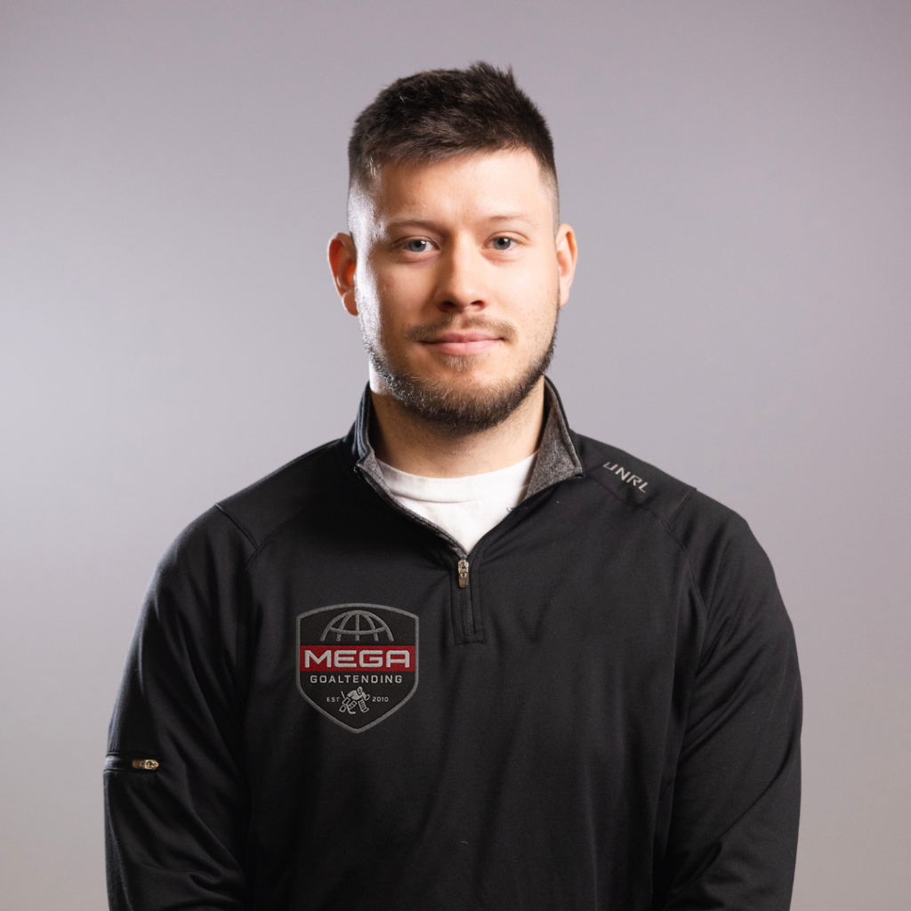 Bearded man facing the camera with a slight smile, wearing a black pullover against a neutral gray background.