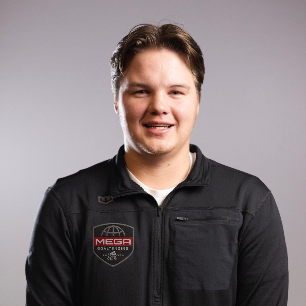 Smiling young man stands facing the camera, wearing a black zip jacket against a neutral gray studio background.